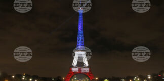 Хора гледат Айфеловата кула, осветена в цветовете на френското знаме в памет на жертвите на атентатите от 13 ноември.