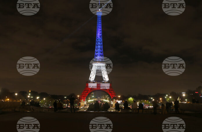 Хора гледат Айфеловата кула, осветена в цветовете на френското знаме в памет на жертвите на атентатите от 13 ноември.