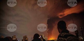 Жители наблюдават пламъци и дим, които се издигат от склад за петрол, поразен при удари срещу Техеран, 7 март 2026 г.