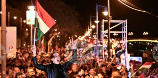 Мъж развява унгарско знаме на фона на празненства по улицте на Будапеща след обявяването на частичните резултати от унгарските парламентарни избори, 12 април 2026 г.