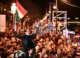 Мъж развява унгарско знаме на фона на празненства по улицте на Будапеща след обявяването на частичните резултати от унгарските парламентарни избори, 12 април 2026 г.