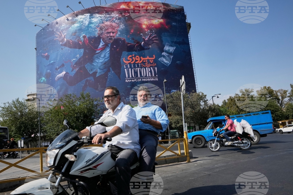 Иранци подминават на мотоциклет билборд в столицата Техеран, изобразяващ президента на САЩ Доналд Тръмп потънал сред експлозии с надпис "Голяма победа! Ормузкият проток", 24 август 2026 г.