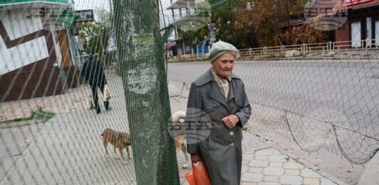 Възрастна жена върви под мрежи срещу дронове, опънати над улица по време на местно прекратяване на огъня, свързано с евакуационни дейности в Олешки, Херсонска област, Украйна на 27 октомври 2026 г.